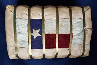 This small bale of cotton was presented to Mrs. Harrison during a Presidential visit to Galveston, Texas, April 18, 1891. It is covered on all sides with a grosgrain silk fabric, but the fabric comes around the two wide sides partially leaving a small 