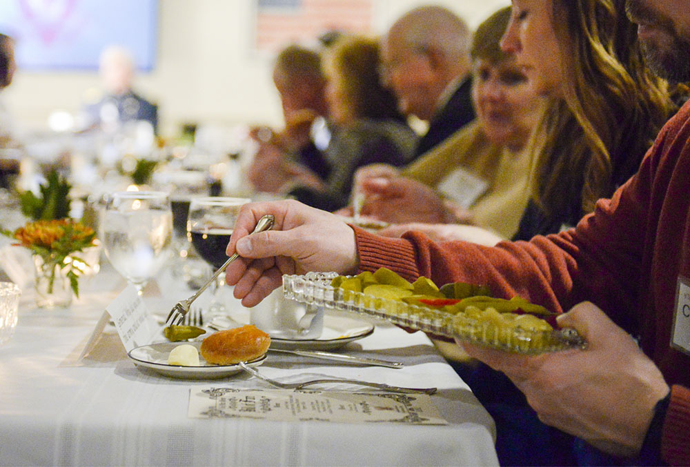 Photograph of a dinner table and a hand putting food on a plate.