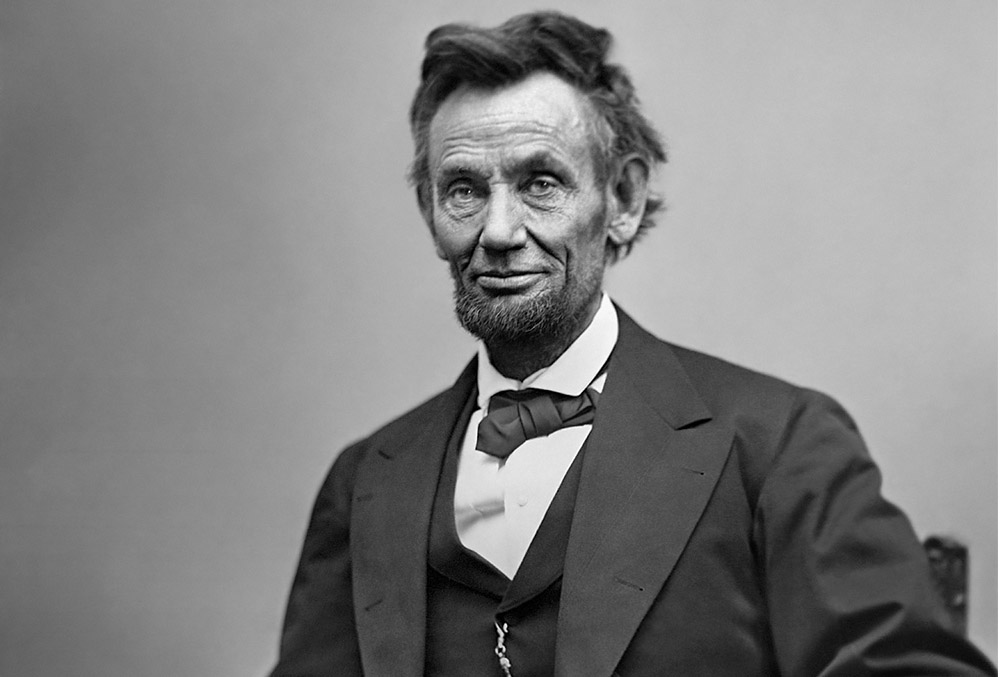Photograph of Abraham Lincoln, whom wears a slight smile on his aged face.