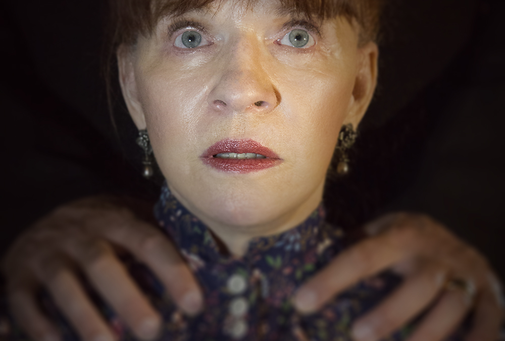 Photograph of a scared woman with a man's hands on her shoulders.