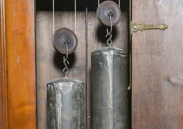 Tall case or grandfather clock made by George Woltz in Hagerstown, Maryland between 1800 and 1812. Clock has moon dial at top and a date dial below the center of the hands, and strikes on the hour. Cherry cabinet with front legs that curve out . There is a spindle on either side of the face. Rounded center at the top with rosette design. Top corners come up to pointed spindles. Clock face is a half circle at top with the dates above the moon dial, Roman numerals and painted floral designs in four corners, and glass door.