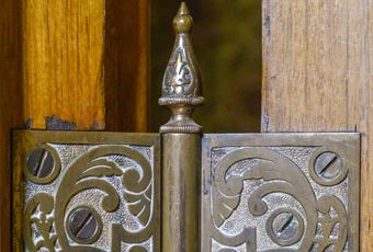 Ornate Victorian door hinge at the Benjamin Harrison Presidential Site. The patterning shows several curves bursting outward from a single origin point. The door hinge shows some signs of age.