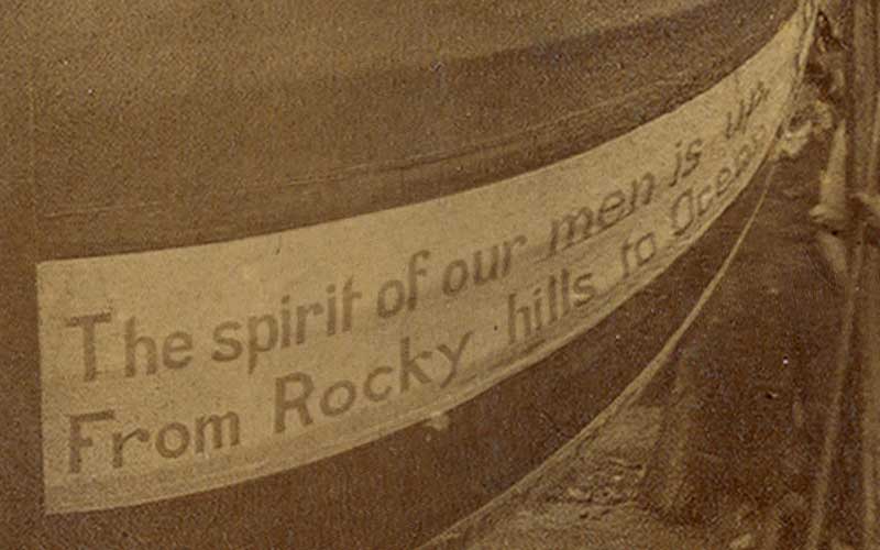 Photograph (sepia tone) mounted on heavy board. Images shows 1888 Campaign Ball with D. E. Brockett (designer and builder) standing to the left with other men behind him and to the right side of the ball. There is also a stack of lumber to the back on the right and a shed type building to the left. Below image on board is the following information: 