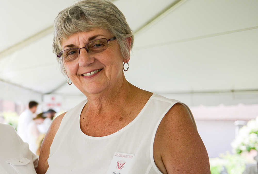 Photo of Martha, president of the volunteer board. She is dressed in white, outdoors during a presidential site event in the spring.