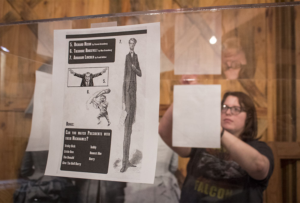 Photograph of a woman taping paper print outs to a tall glass cube.
