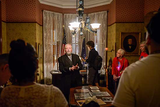photograph of an actor playing benjamin harrison, conferring with a tour group in his office space.