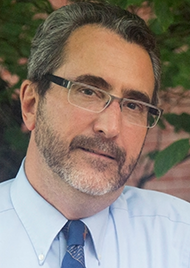 Portrait of Ellis Hall. A middle aged man with dark hair, a short beard, and rectangular glasses.