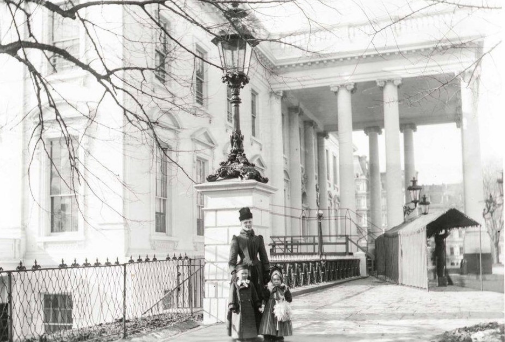 Photo by Frances Benjamin Johnson of Mary Russel Harrison in front of a large government building, accompanied by two children at her heel.